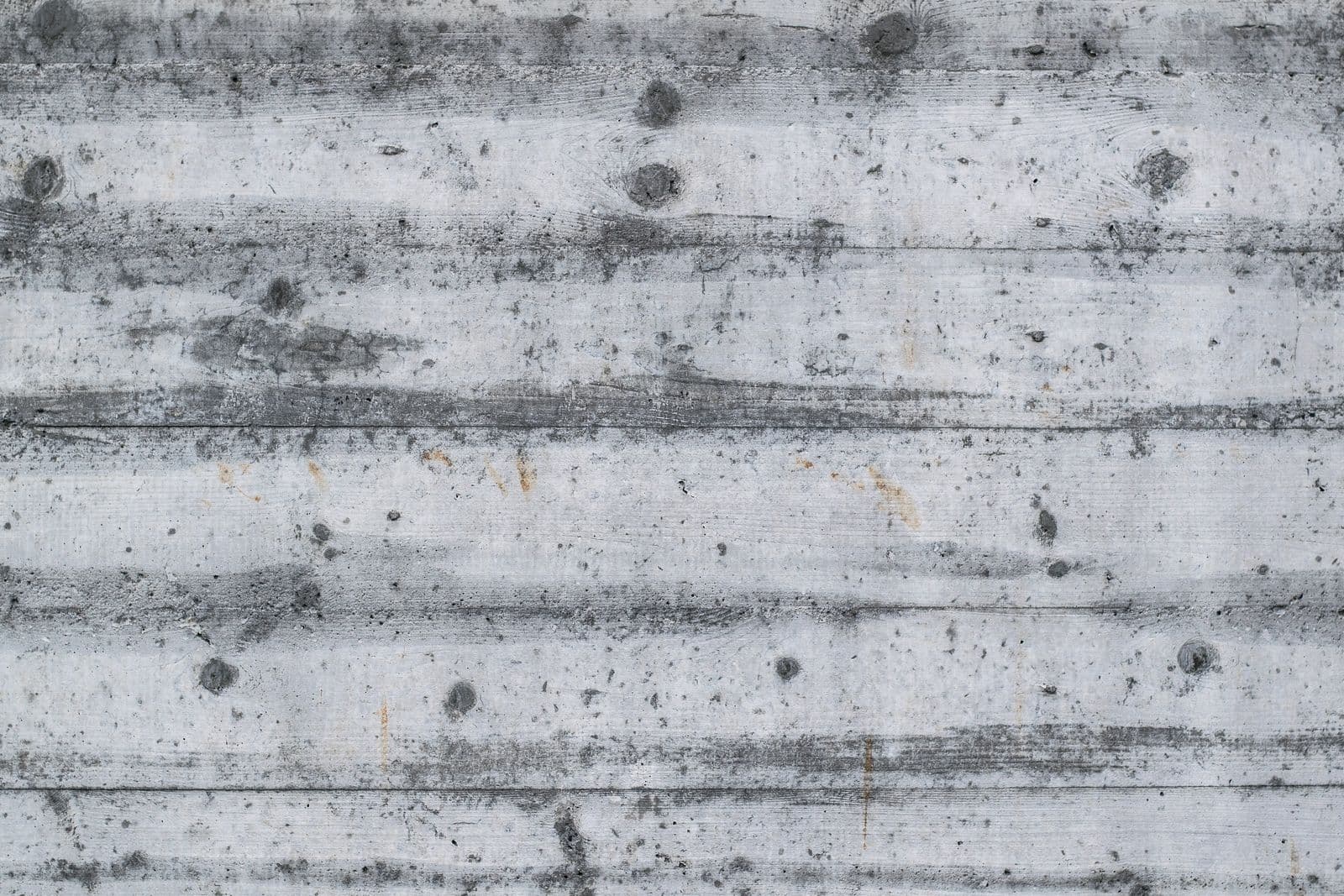 Mur en béton brut de décoffrage : empreinte horizontale des planches de coffrage, trous de banche et bullage, teinte grise.
