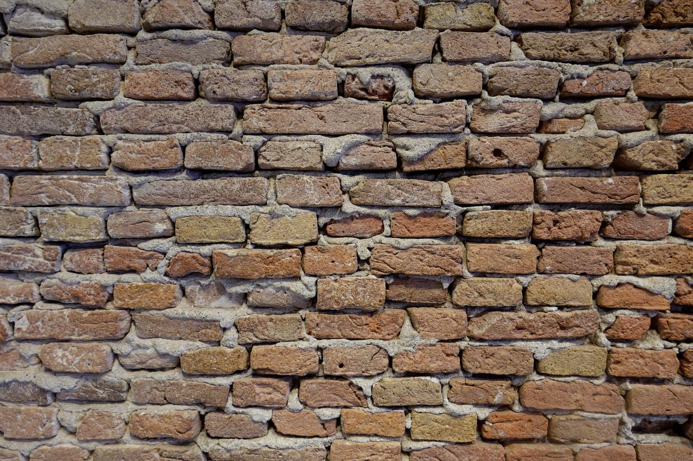 Mur de brique ancienne aux teintes ocre et rouge, joints de mortier de chaux épais et irréguliers.