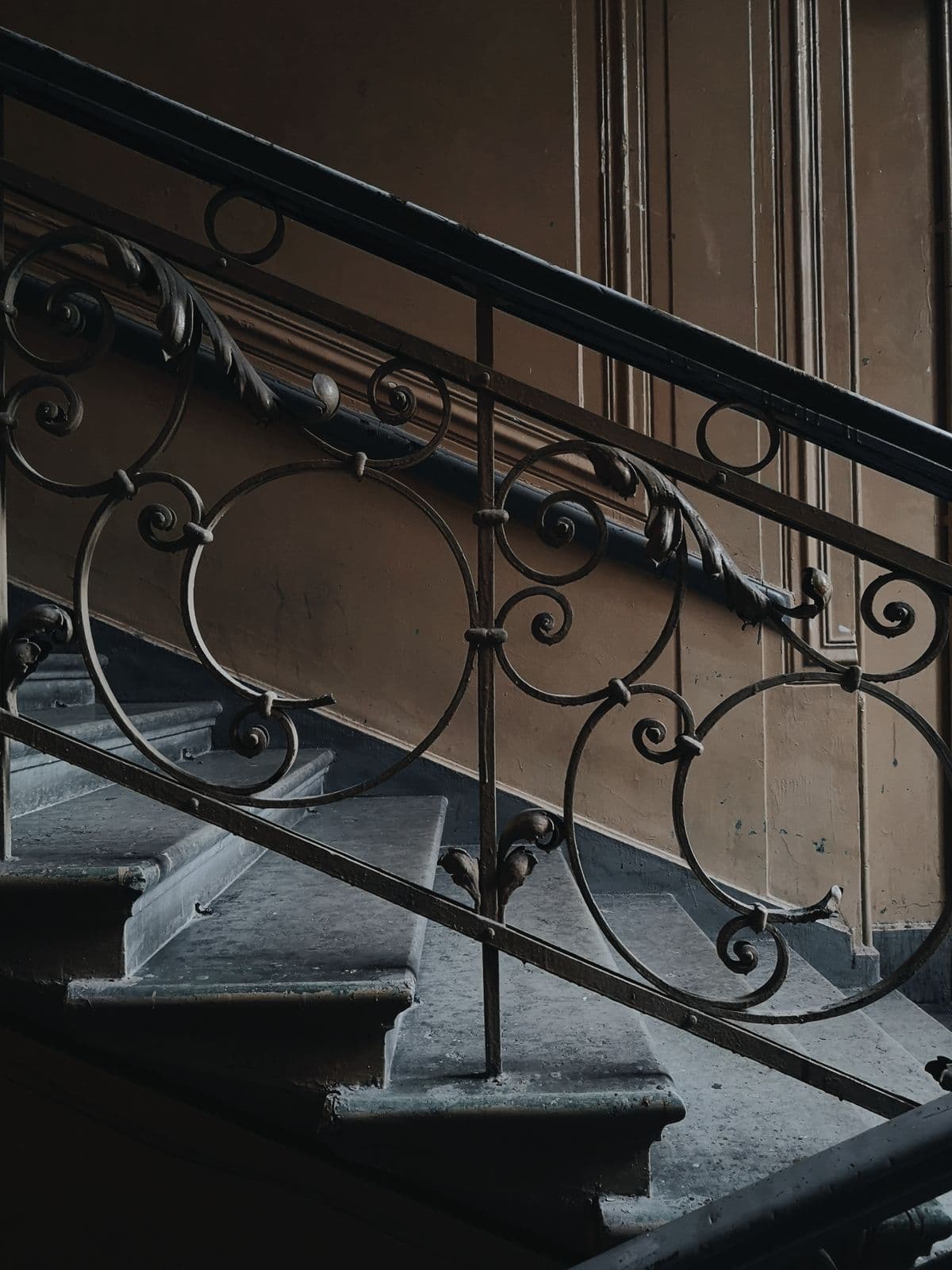 Entrée d'immeuble : départ d'escalier et rampe en fer forgé, sol en mosaïque.