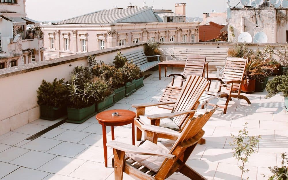 Terrasse en toiture d'un immeuble ancien : dalles claires, transats en bois et jardinières, au-dessus de l'étanchéité.