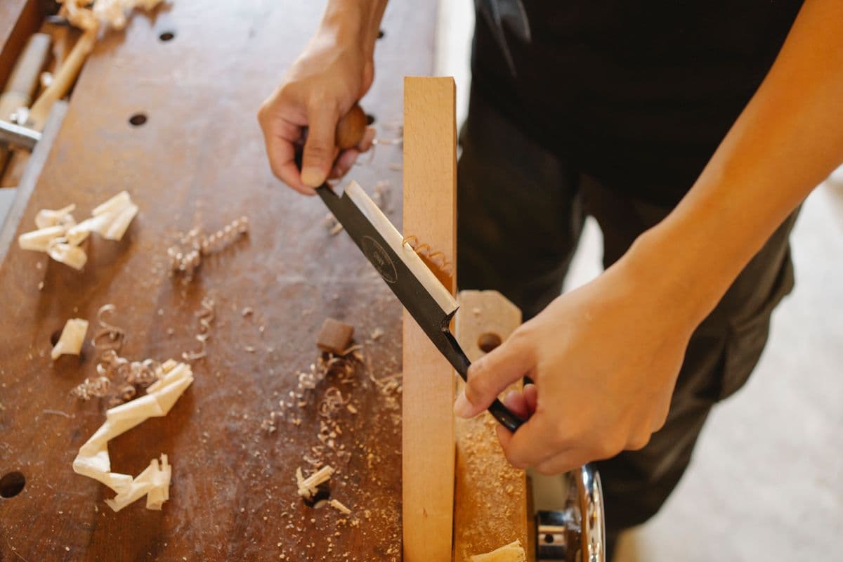 Menuisier travaillant une pièce de bois au ciseau et au maillet, en atelier.