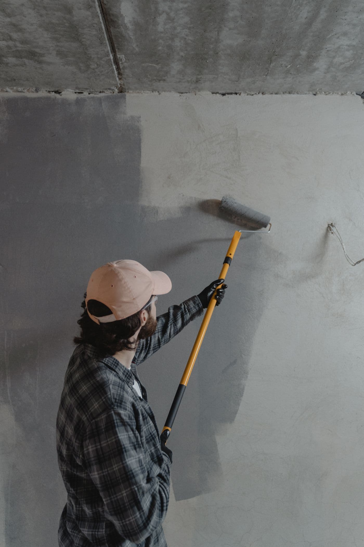 Peintre appliquant une sous-couche au rouleau sur perche sur un mur brut, en rénovation intérieure.