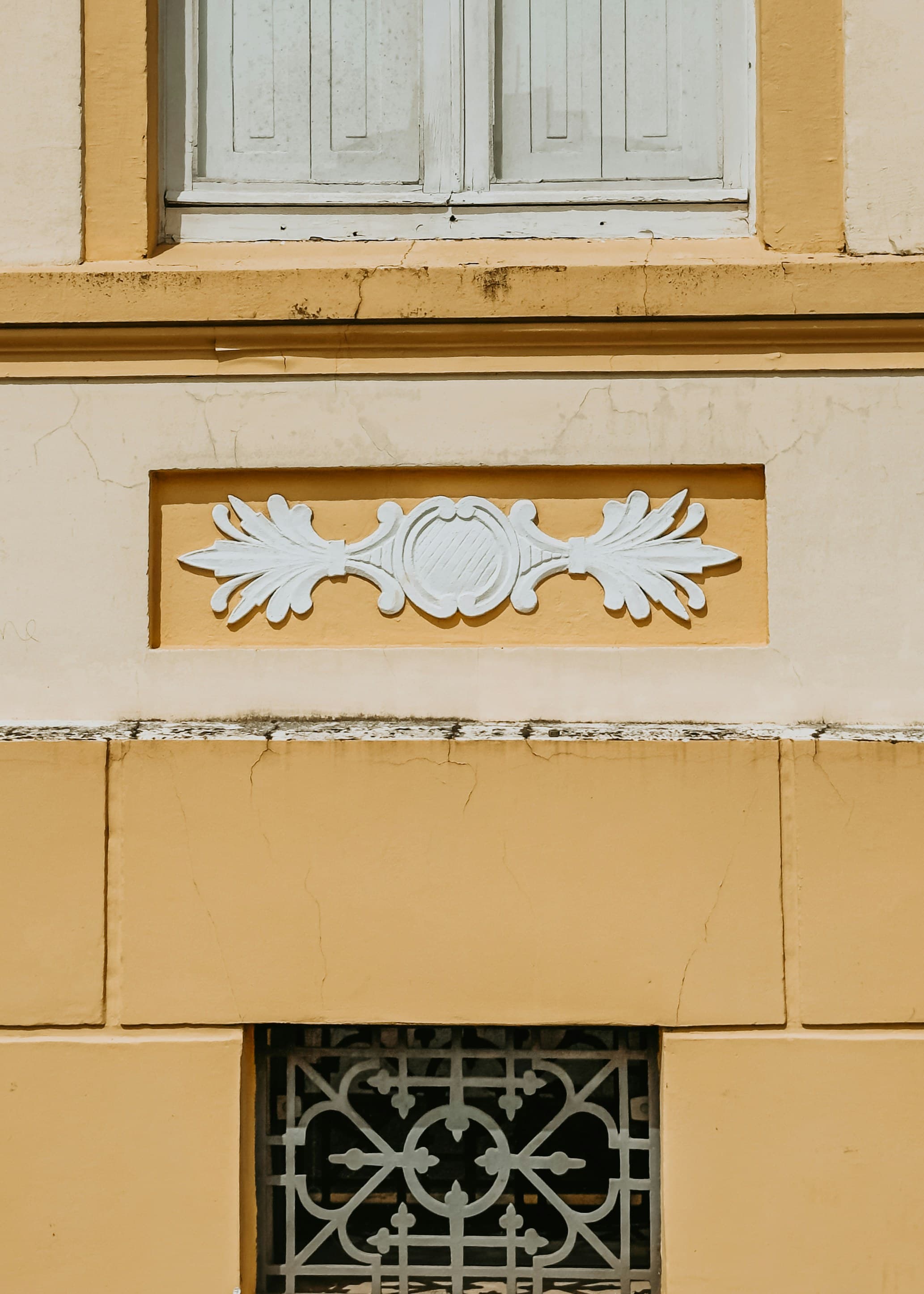 Détail d'une façade enduite en ocre avec ornementation en plâtre et moulures filantes.