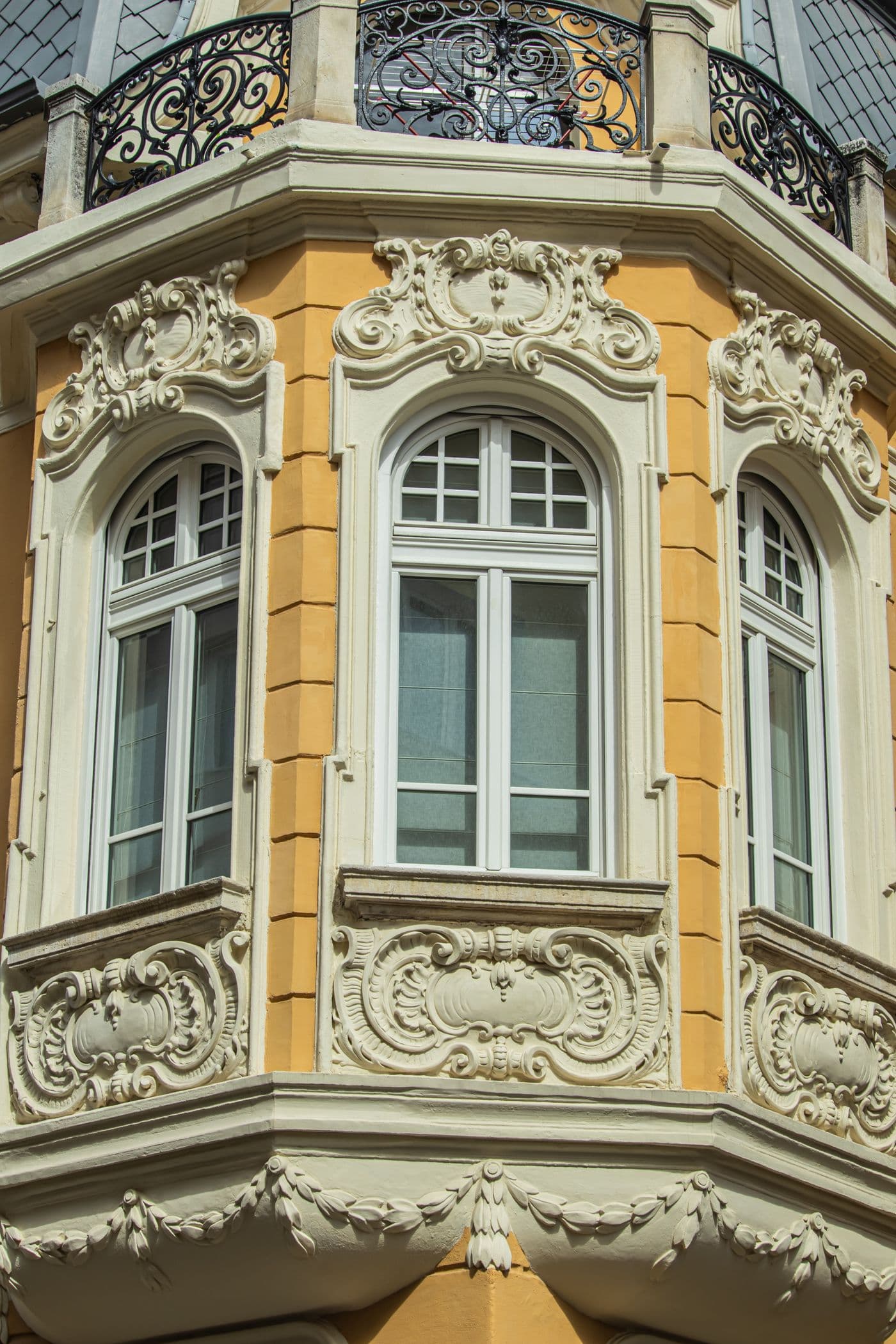 Façade enduite en ocre à modénature en plâtre blanc : cartouches, guirlandes et encadrements rocaille autour de fenêtres cintrées.