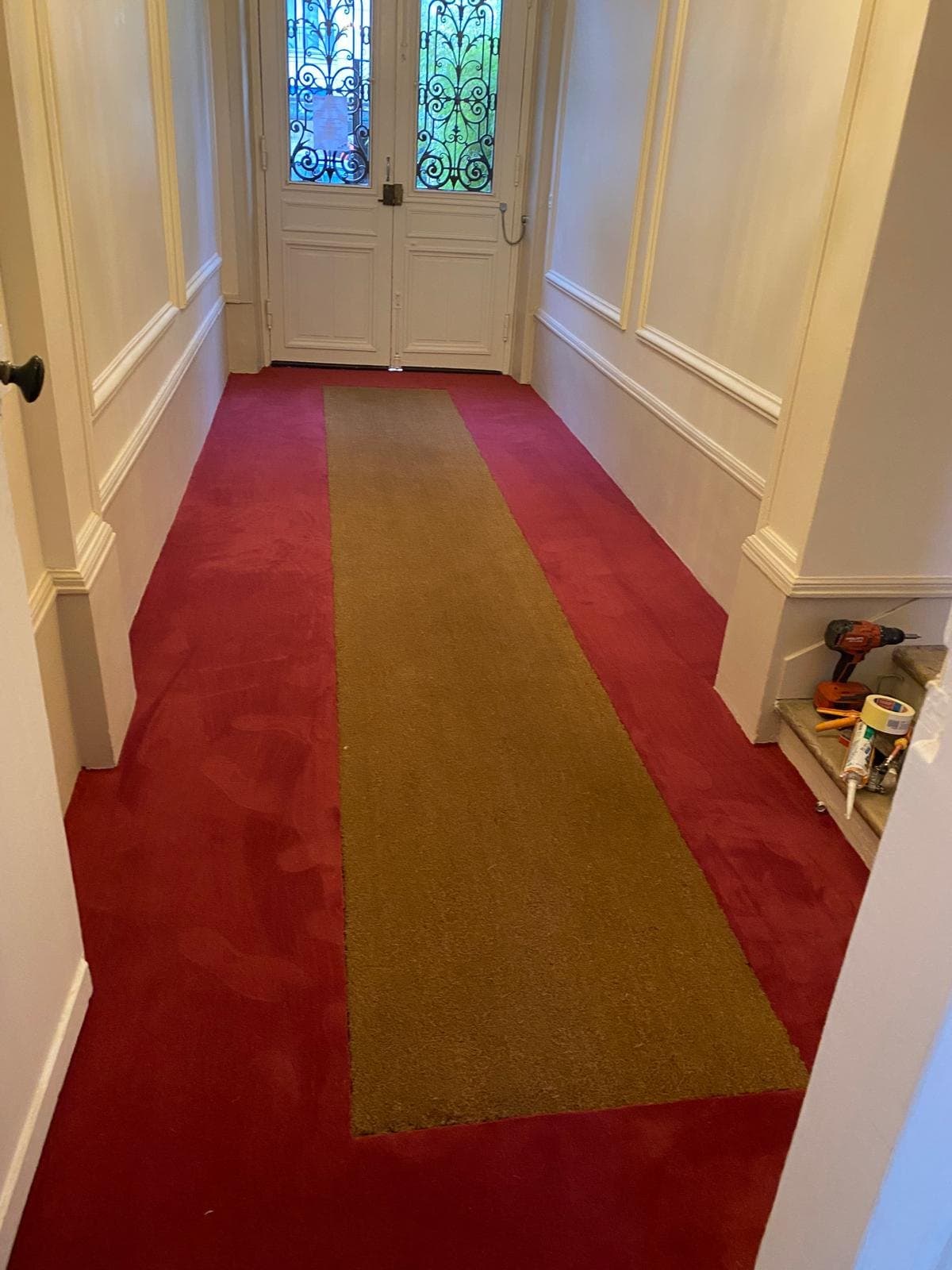 Couloir d'immeuble rénové, tapis et porte à vitrail.