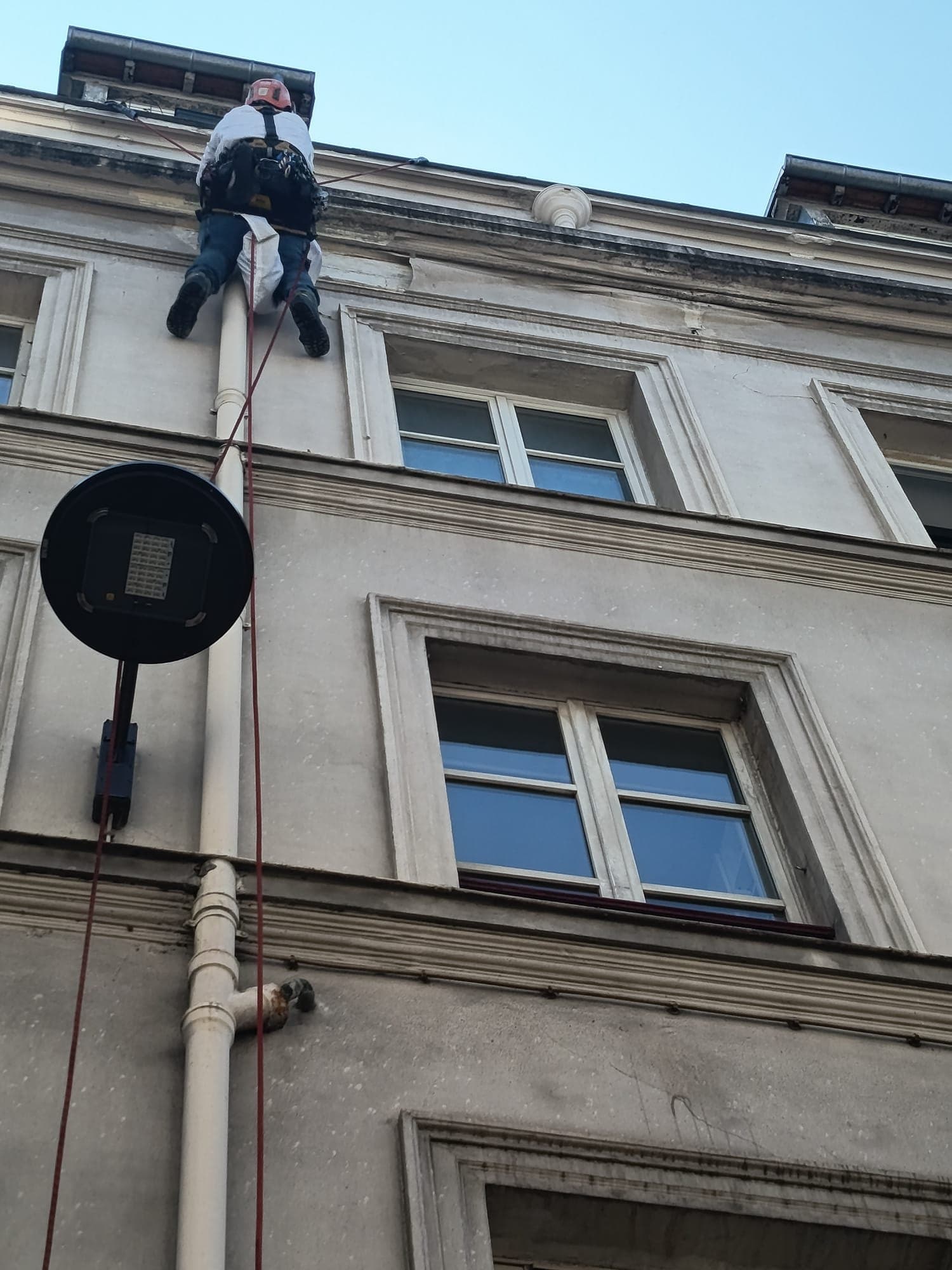 Technicien cordiste suspendu devant une fenêtre d'immeuble.
