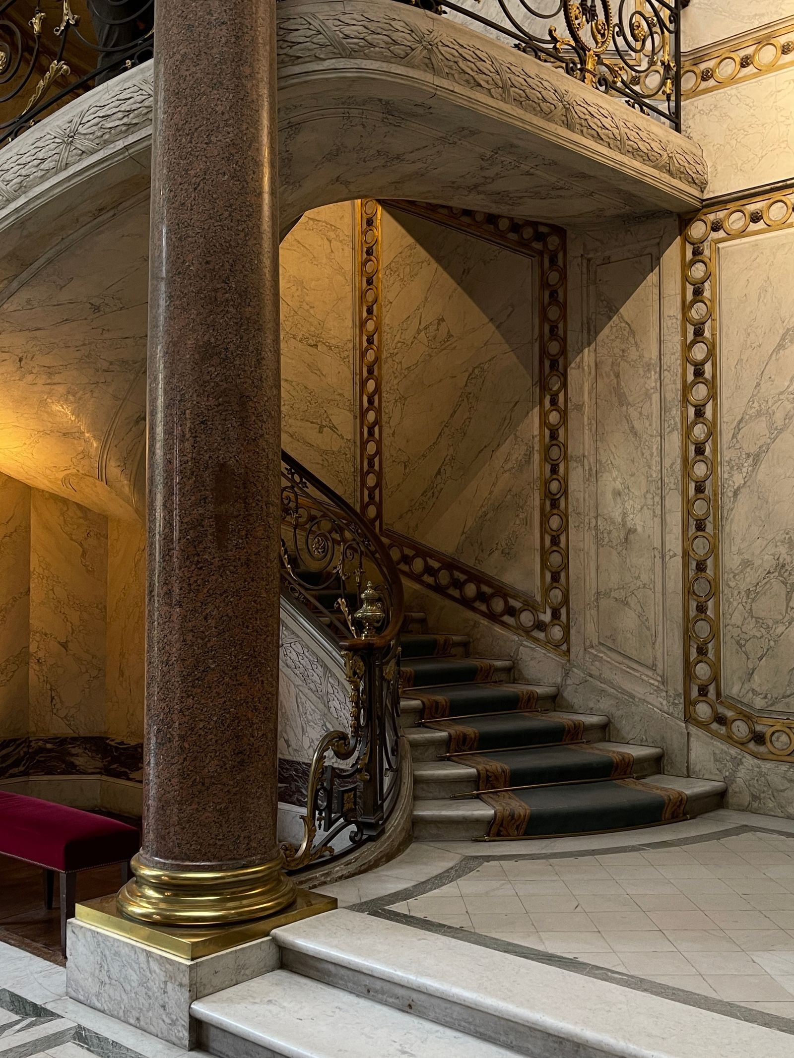 Cage d'escalier d'un immeuble ancien : escalier en colimaçon à marches de pierre et de marbre, rampe ouvragée et colonne.