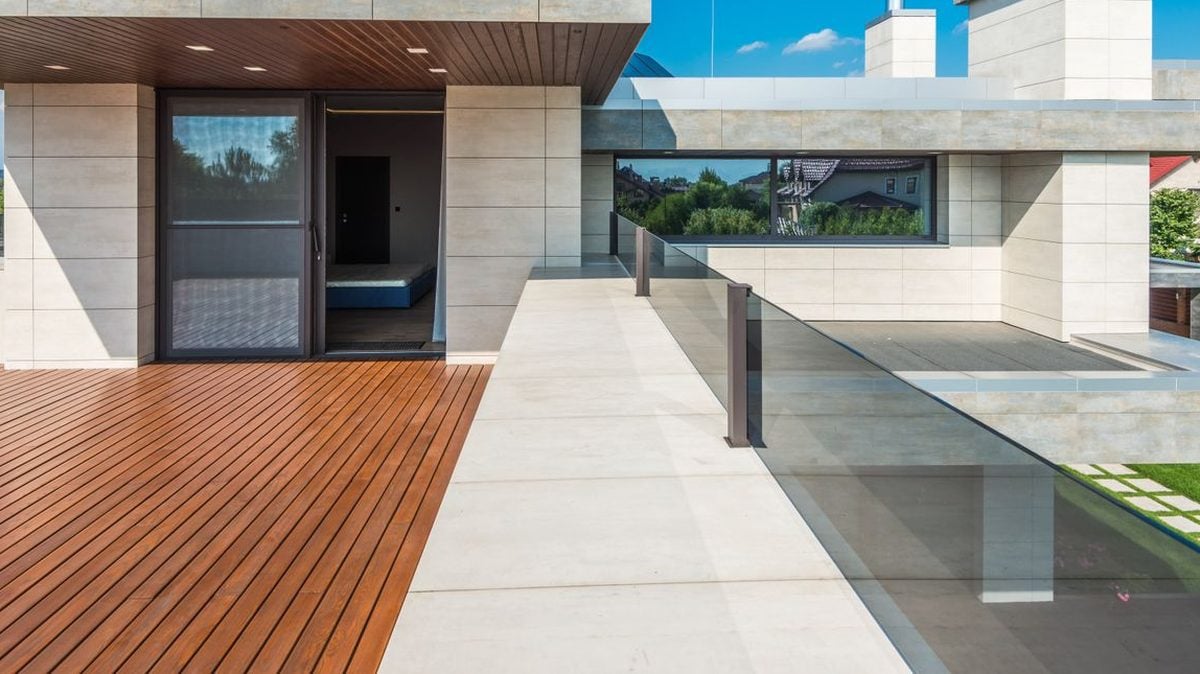 Toiture-terrasse moderne : platelage bois et dalles de pierre claire bordés d'un garde-corps vitré, au-dessus de l'étanchéité.