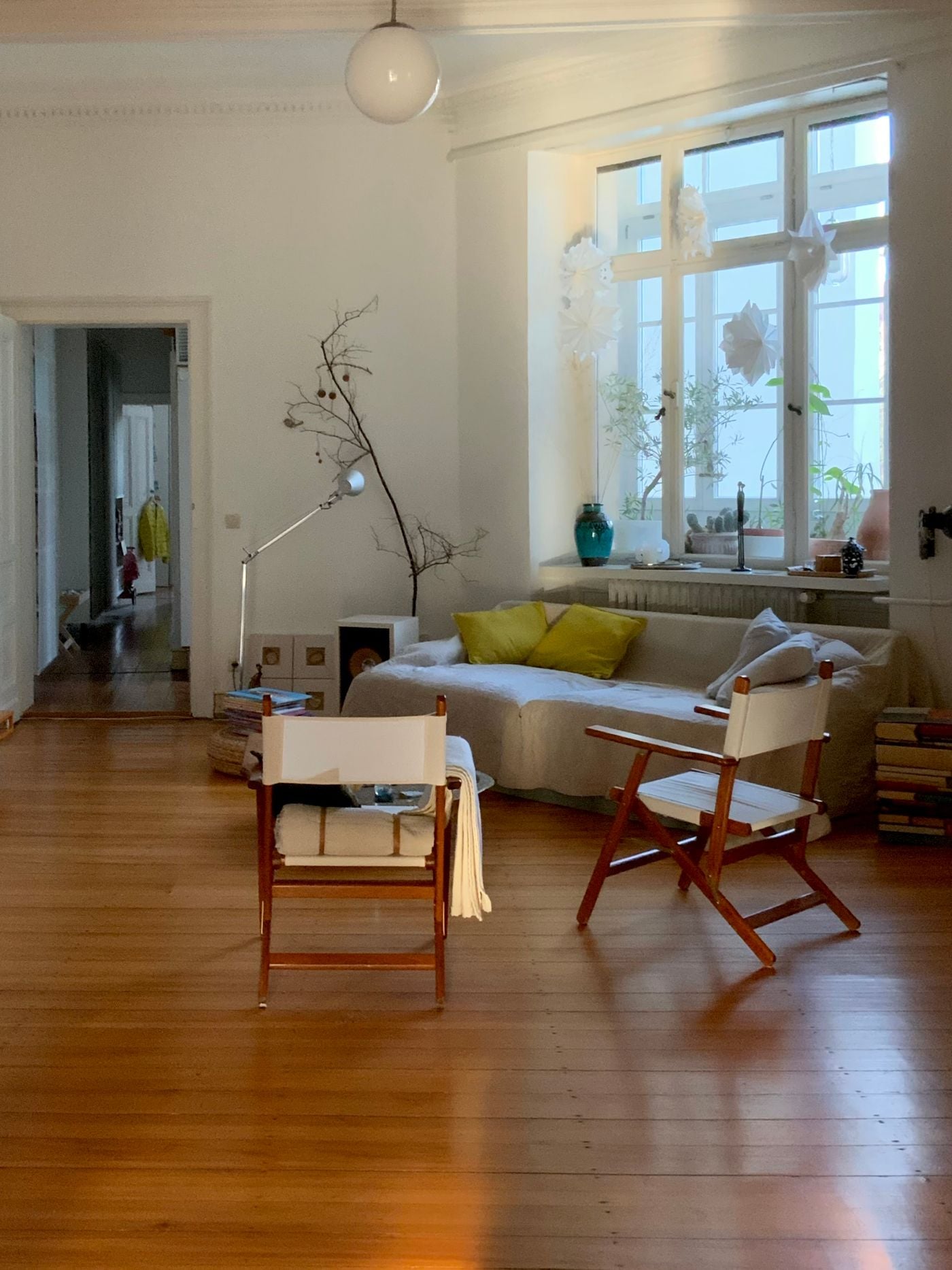 Séjour de maison rénovée : salon lumineux aux tons chauds, fauteuils en bois, plantes et grandes fenêtres.