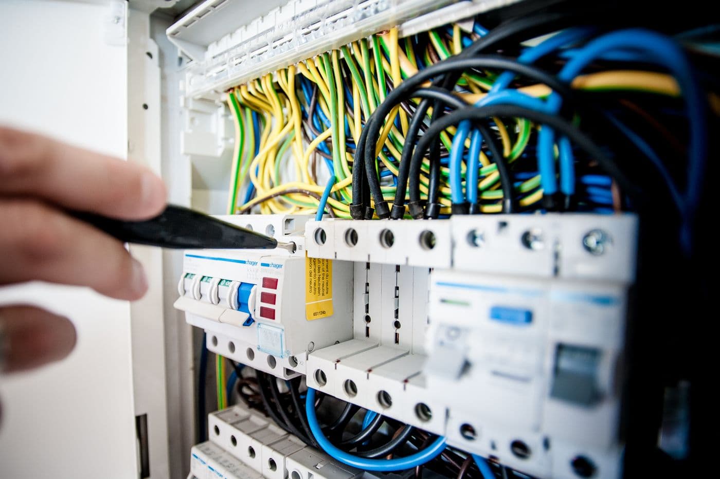 Main d'un électricien intervenant sur un tableau électrique ouvert : disjoncteurs modulaires et câblage, en cours de mise aux normes.