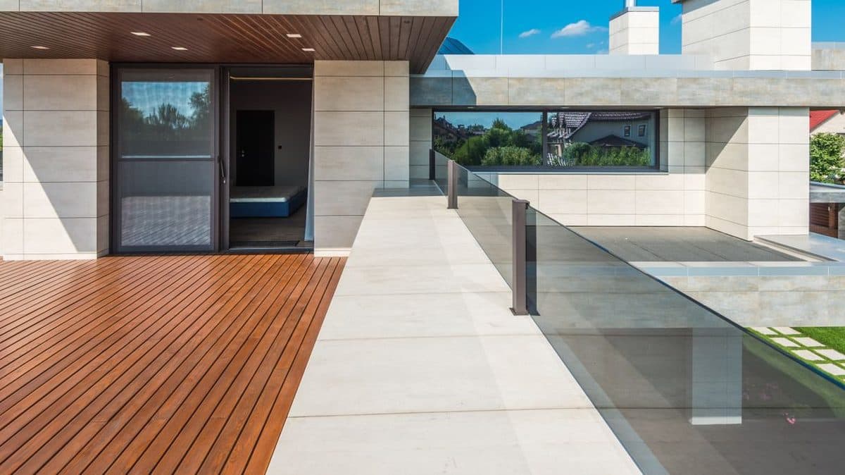 Toiture-terrasse moderne : platelage bois et dalles de pierre claire bordés d'un garde-corps vitré, au-dessus de l'étanchéité.