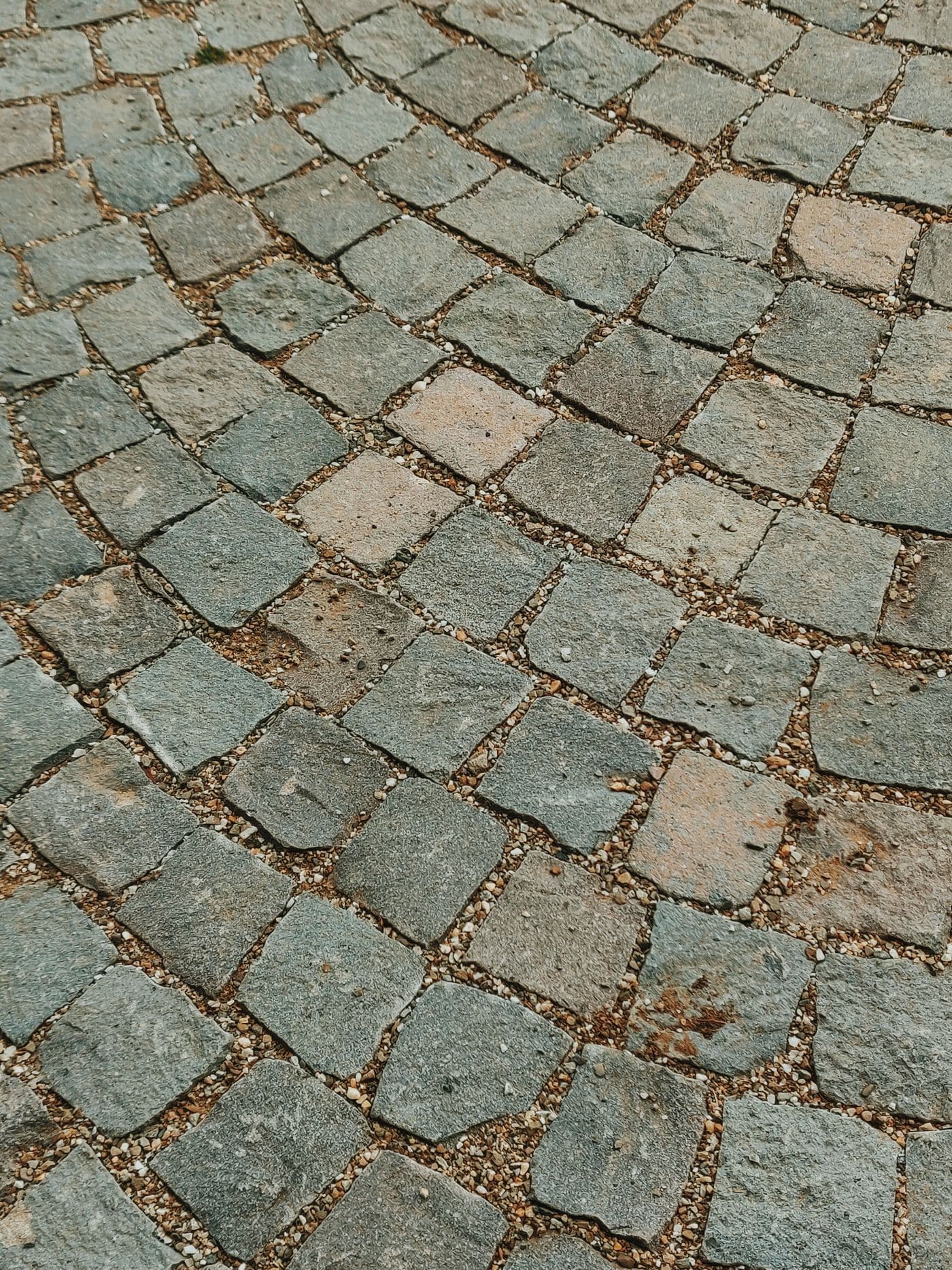 Pavés de pierre clairs à joints de sable et gravier, vue rasante sur le calepinage d'un sol extérieur.