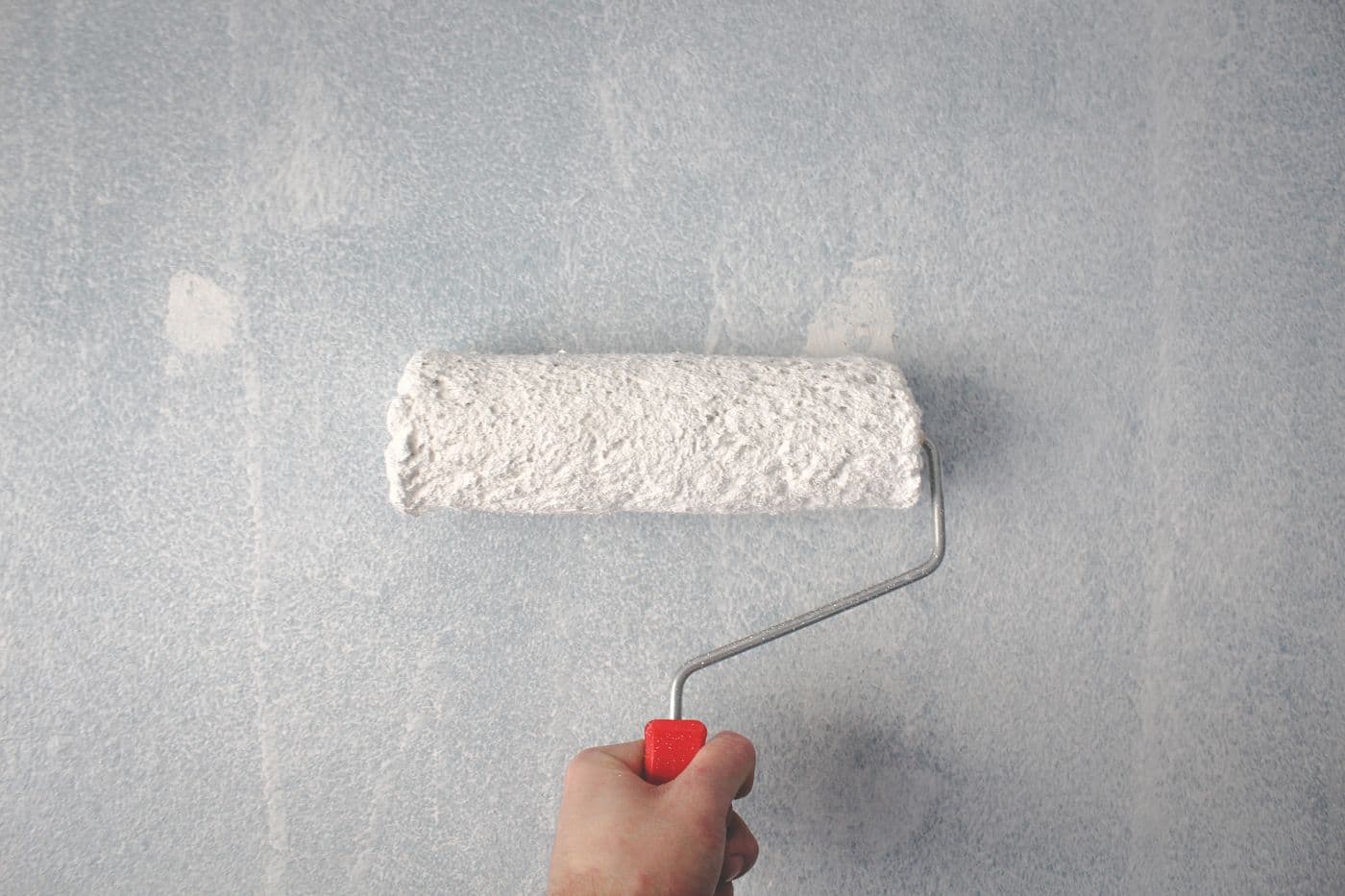 Gros plan d'un rouleau chargé de peinture blanche appliquée sur un mur en cours de mise en peinture.