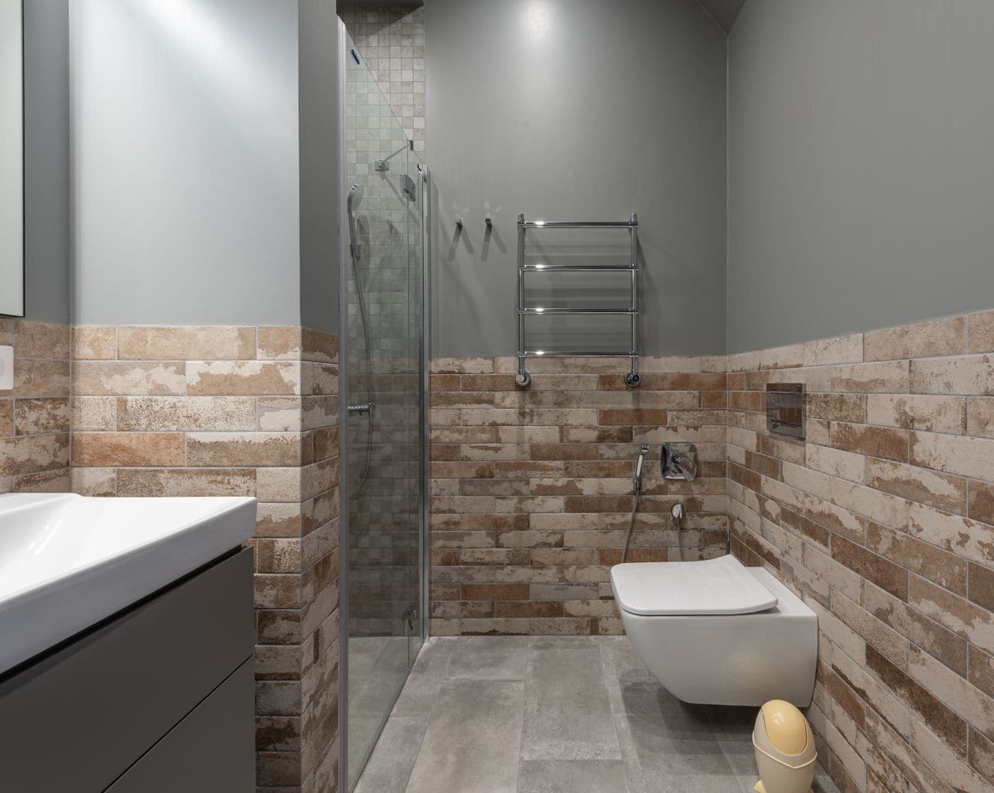 Salle de bains à douche à l'italienne vitrée, faïence effet brique aux tons terre, WC suspendu et sèche-serviettes.